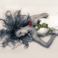 Черно-белое фото с девушкой, которая лежит на полу с красной розой