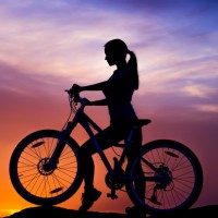 Силуэт с девушкой на велосипеде на фоне заката