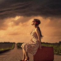 Девушка в платье сидит на чемодане на дороге